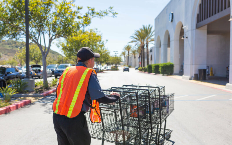 A client pushes shopping carts in a parking lot outside the grocery store.